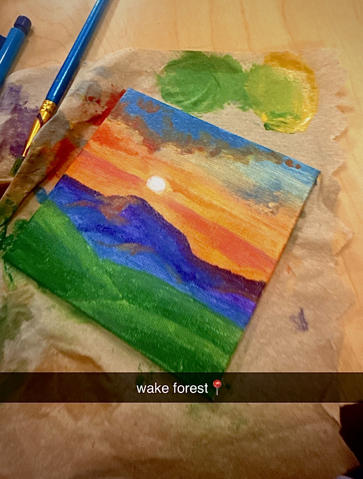 Small acrylic painting of a sunrise over blue mountains above a green field